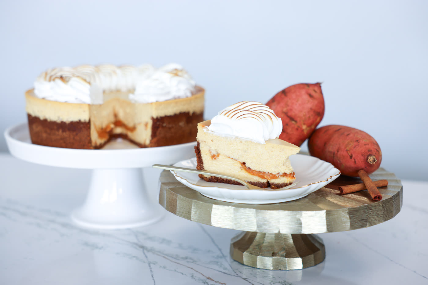 Sweet potato cheesecake with a toasted topping beside fresh sweet potatoes and cinnamon sticks