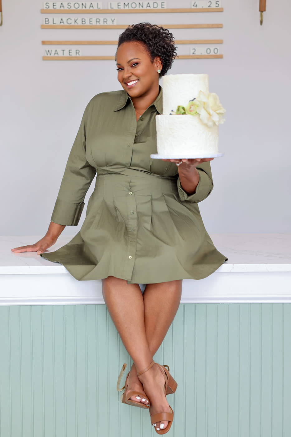 Yodith, founder of Yodith's Cakery, smiling in the bakery with a two-tier white cake